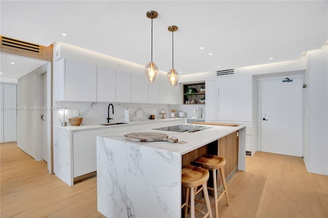 kitchen with tasteful backsplash, decorative light fixtures, light hardwood / wood-style flooring, a center island, and white cabinets