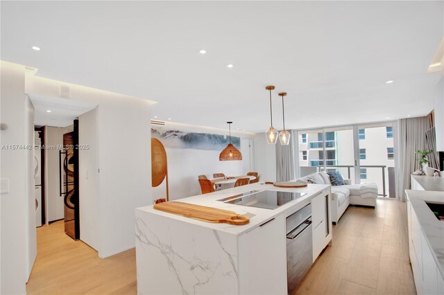 kitchen featuring a center island, decorative light fixtures, light stone countertops, white cabinets, and light hardwood / wood-style flooring