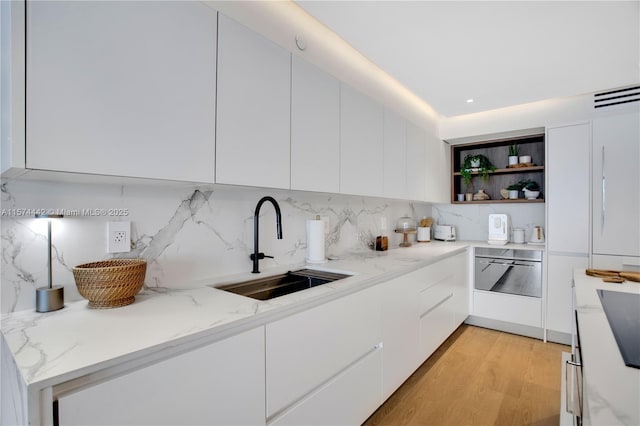 kitchen with light wood-type flooring, light stone countertops, decorative backsplash, sink, and white cabinets