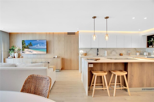 kitchen featuring white cabinetry, sink, a kitchen breakfast bar, decorative light fixtures, and light wood-type flooring