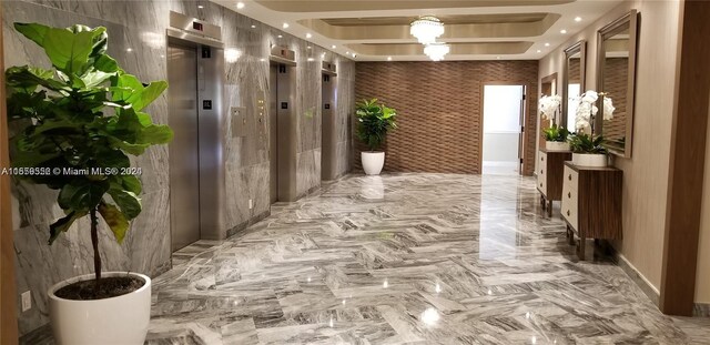 hallway featuring elevator, tile walls, and a raised ceiling