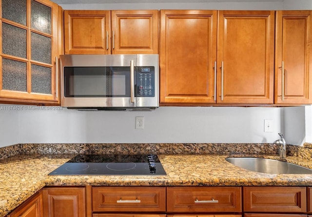 kitchen featuring black electric stovetop, sink, and light stone counters