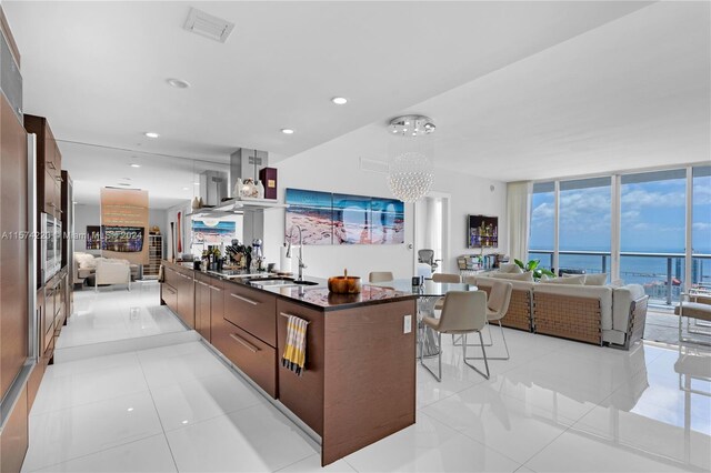 kitchen featuring a water view, light tile floors, sink, island range hood, and a center island with sink