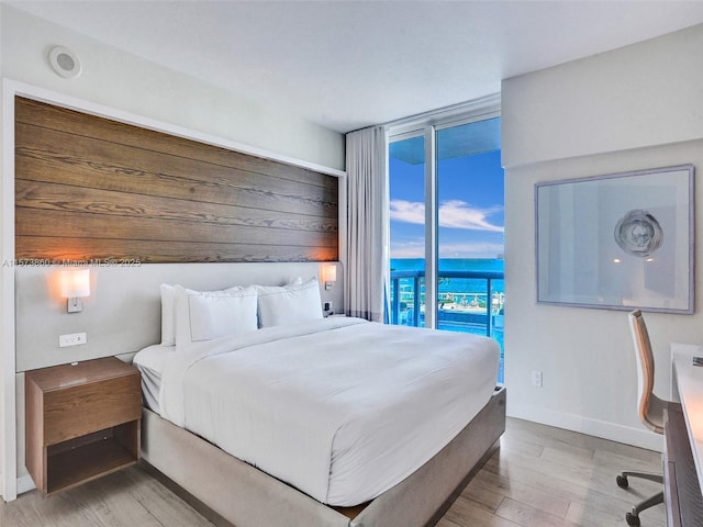 bedroom with expansive windows, access to outside, and light hardwood / wood-style flooring