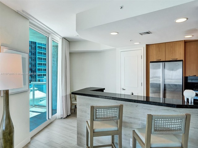 kitchen with light hardwood / wood-style flooring, stainless steel refrigerator, and kitchen peninsula