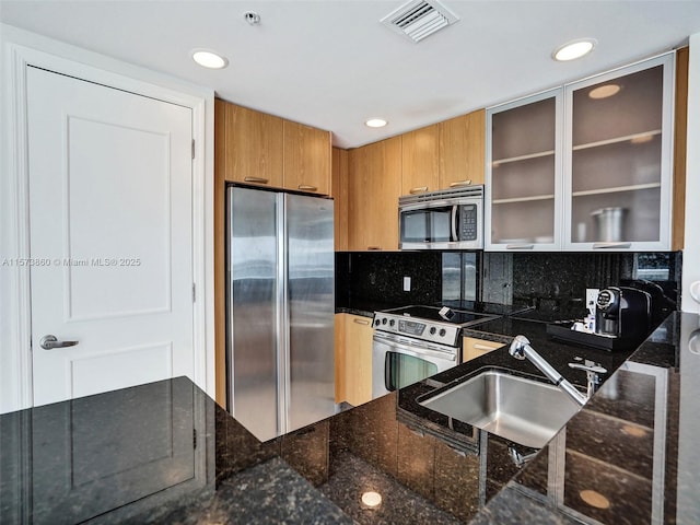 kitchen with stainless steel appliances, sink, decorative backsplash, and dark stone counters