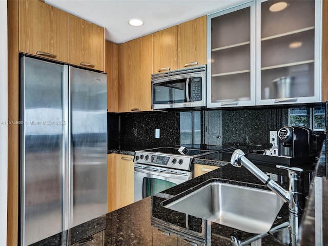 kitchen featuring stainless steel appliances, sink, backsplash, and dark stone counters