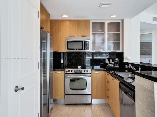 kitchen featuring tasteful backsplash, sink, dark stone countertops, light hardwood / wood-style floors, and stainless steel appliances