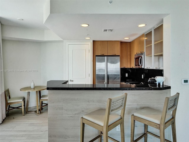 kitchen featuring light hardwood / wood-style flooring, a breakfast bar, backsplash, stainless steel appliances, and kitchen peninsula