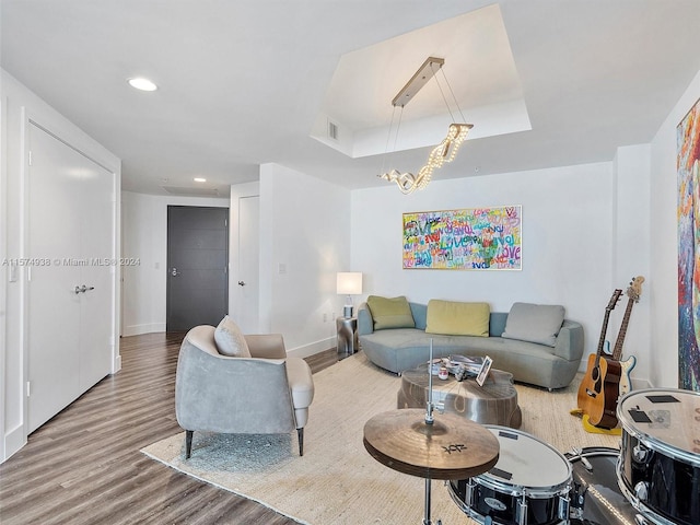 living room featuring wood-type flooring, a raised ceiling, and an inviting chandelier