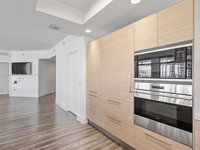 kitchen featuring light wood-type flooring, black microwave, stainless steel oven, and light brown cabinetry