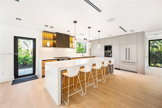 kitchen with custom exhaust hood, decorative light fixtures, a breakfast bar, light wood-type flooring, and a kitchen island