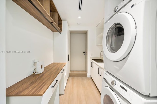 washroom with light hardwood / wood-style flooring, stacked washer / dryer, sink, and cabinets