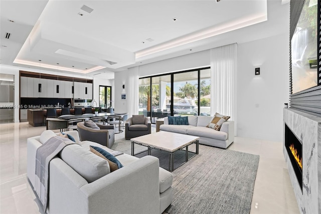 living room featuring light tile flooring, a fireplace, and a tray ceiling