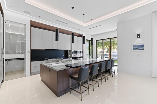 kitchen with pendant lighting, light stone countertops, a breakfast bar area, light tile floors, and a center island with sink