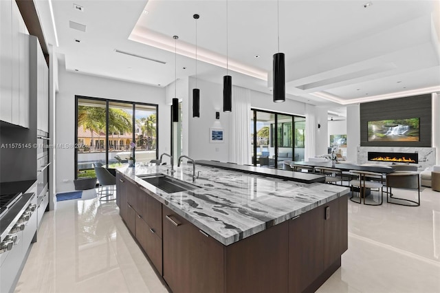 kitchen featuring a large fireplace, sink, light tile floors, and a tray ceiling