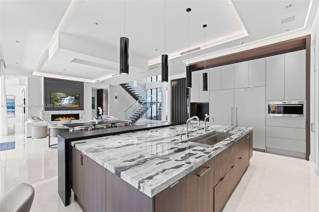 kitchen featuring a spacious island, a large fireplace, a tray ceiling, sink, and pendant lighting