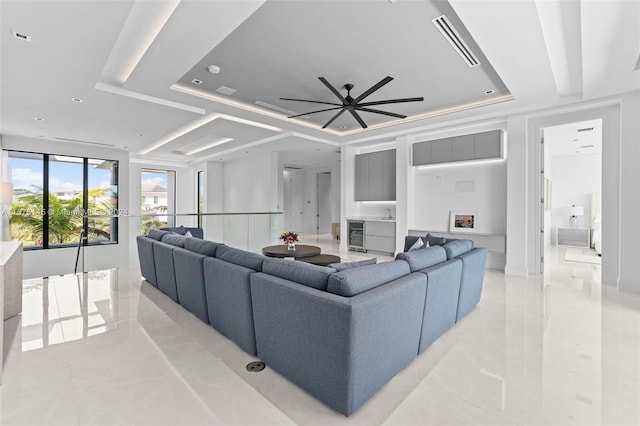 living room with a raised ceiling, ceiling fan, and light tile floors