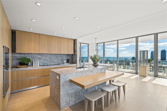 kitchen with an island with sink, modern cabinets, backsplash, and a sink