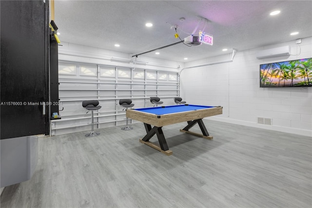 game room featuring an AC wall unit, light hardwood / wood-style floors, pool table, and a textured ceiling