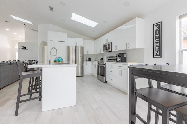 kitchen featuring hanging light fixtures, stainless steel appliances, a skylight, and white cabinets