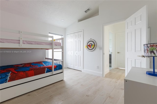 bedroom featuring lofted ceiling, light hardwood / wood-style floors, a closet, and a textured ceiling