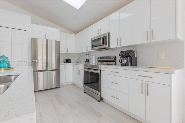 kitchen with white cabinetry, lofted ceiling with skylight, tasteful backsplash, light wood-type flooring, and stainless steel appliances