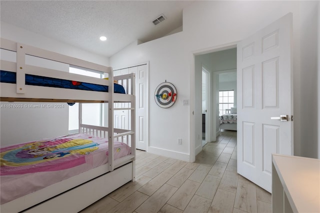 bedroom featuring light wood-type flooring, a closet, vaulted ceiling, and a textured ceiling