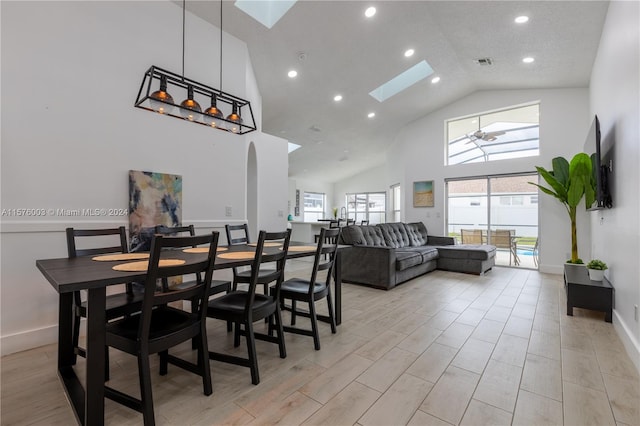 dining space with a skylight, ceiling fan, high vaulted ceiling, and light hardwood / wood-style floors