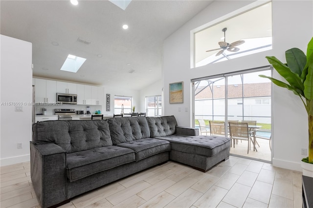 living room featuring a skylight, a healthy amount of sunlight, ceiling fan, and high vaulted ceiling