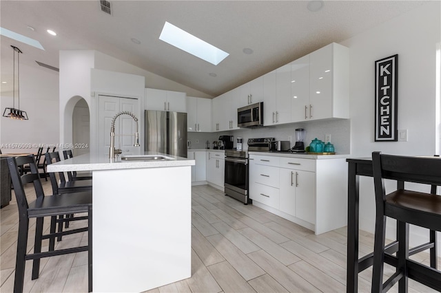 kitchen featuring tasteful backsplash, stainless steel appliances, pendant lighting, white cabinets, and vaulted ceiling with skylight