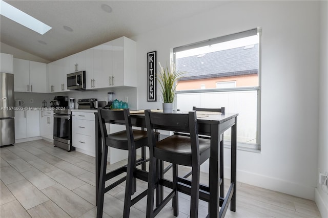 kitchen with lofted ceiling with skylight, white cabinetry, stainless steel appliances, and light hardwood / wood-style floors