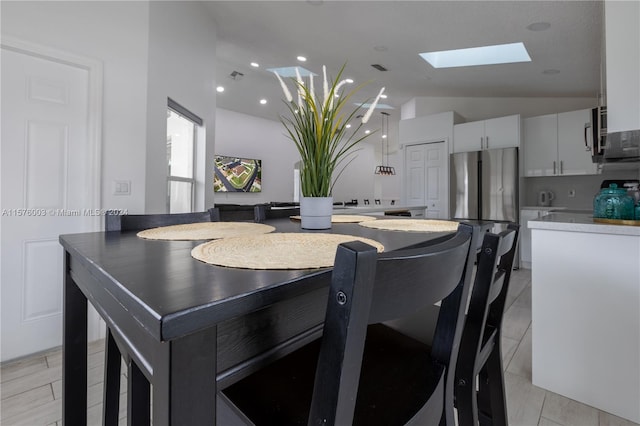 tiled dining space featuring lofted ceiling with skylight