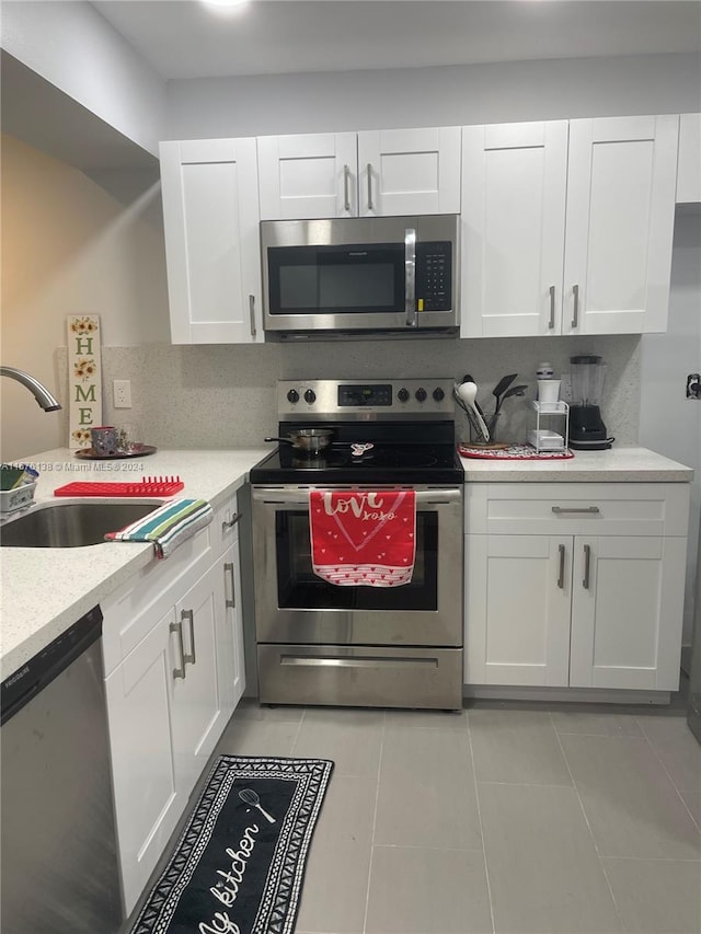 kitchen featuring appliances with stainless steel finishes, tasteful backsplash, white cabinets, sink, and light tile floors