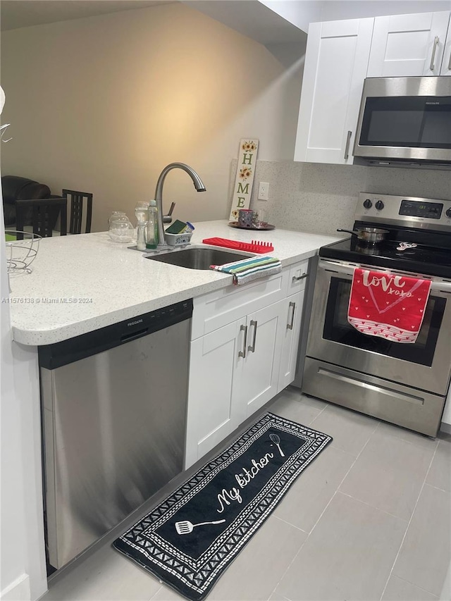 kitchen featuring appliances with stainless steel finishes, sink, light tile flooring, and white cabinetry