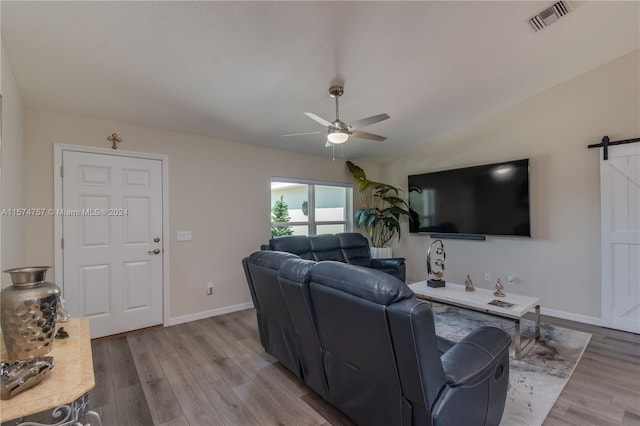 living room with a barn door, ceiling fan, and light wood-type flooring