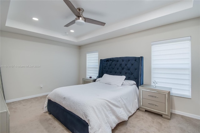 carpeted bedroom with ceiling fan and a tray ceiling