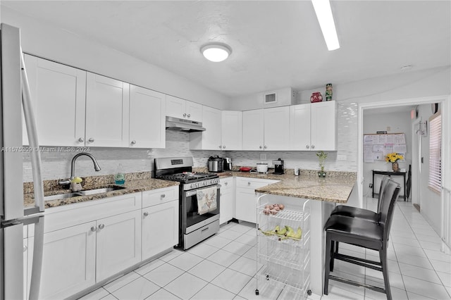 kitchen with white cabinetry, stainless steel range with gas stovetop, light stone counters, sink, and light tile floors