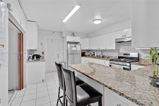 kitchen with appliances with stainless steel finishes, backsplash, light stone counters, white cabinets, and light tile floors