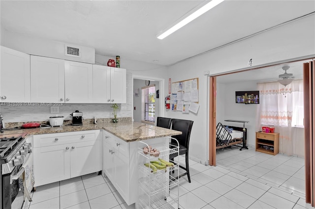 kitchen featuring gas range, white cabinetry, light tile floors, light stone counters, and tasteful backsplash