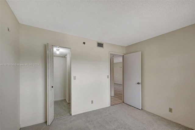 unfurnished bedroom featuring a closet, a textured ceiling, and light colored carpet