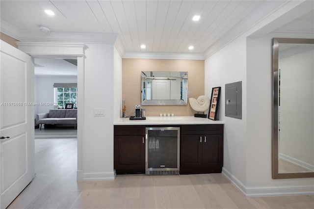 bar featuring wine cooler, dark brown cabinets, ornamental molding, and light wood-type flooring