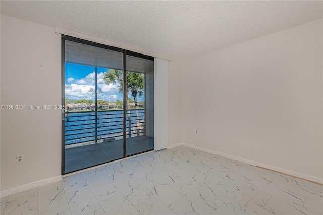 empty room with a wall of windows, marble finish floor, a textured ceiling, and baseboards