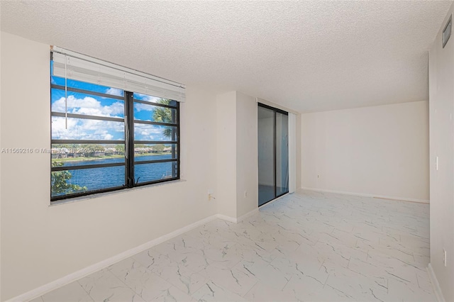 empty room featuring a textured ceiling, marble finish floor, a water view, and baseboards