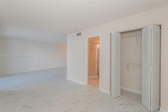 unfurnished bedroom featuring a textured ceiling, visible vents, baseboards, marble finish floor, and a closet