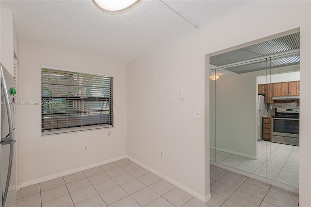 empty room with a textured ceiling, baseboards, and light tile patterned floors