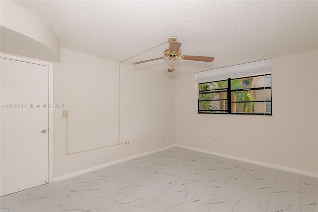 spare room featuring marble finish floor, ceiling fan, baseboards, and a textured ceiling