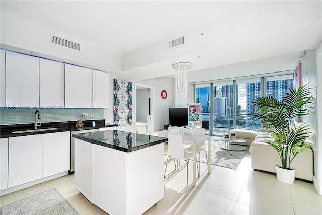 kitchen featuring white cabinets, light tile flooring, sink, a kitchen island, and tasteful backsplash