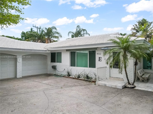 single story home featuring concrete driveway, a tile roof, an attached garage, and stucco siding