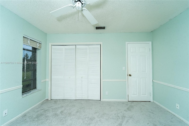 unfurnished bedroom featuring ceiling fan, light colored carpet, a textured ceiling, and a closet